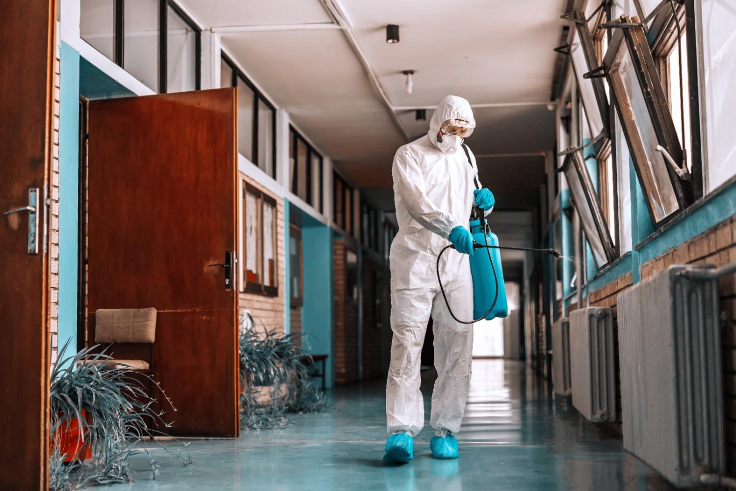 full-length-worker-sterile-uniform-with-face-mask-holding-sprayer-with-disinfectant-spraying-school-hallway (1)